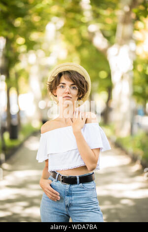 Giovane donna che indossa cappello di paglia che mostra i suoi denti mentre passeggiate nel parco verde Foto Stock