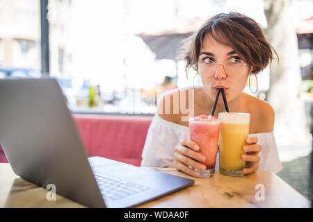 Lifestyle Moda Ritratto di giovane ragazza piuttosto bere il frullato al cafe' all'aperto. Sorridente e godendo di pasto. Indossando Elegante cappello di paglia, occhiali da sole Foto Stock