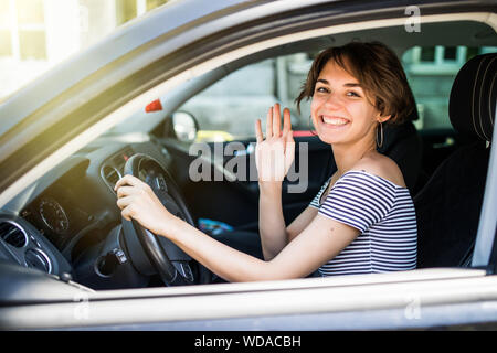 Bella giovane allegro donne guardando la fotocamera con il sorriso e sventolare mentre è seduto nella sua auto Foto Stock