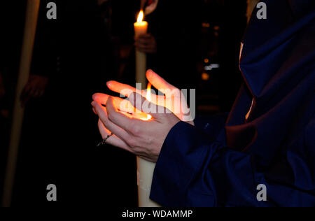 Primo piano delle mani di un nazareno penitente durante una processione notturna tenendo la sua candela. La Settimana Santa di Siviglia, in Andalusia, Spagna Foto Stock