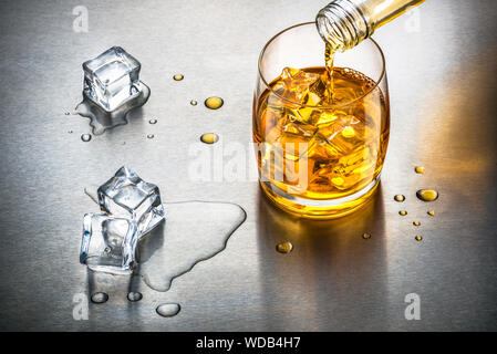 Versando il whisky in glasss con ghiaccio su sfondo metallico close up Foto Stock