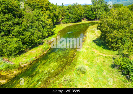 Bellissimo fiume Gacka che scorre tra gli alberi e i campi, summer view, Lika regione della Croazia, drone volando sopra la superficie del fiume Foto Stock