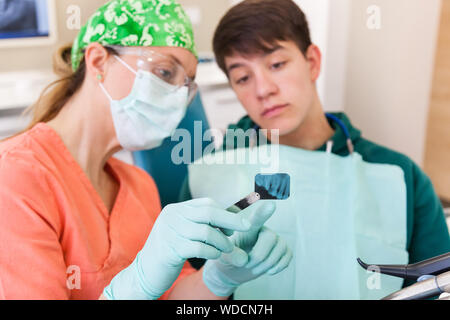 Dentista mostra raggi x al paziente giovane in dentistico, cercando gravi Foto Stock