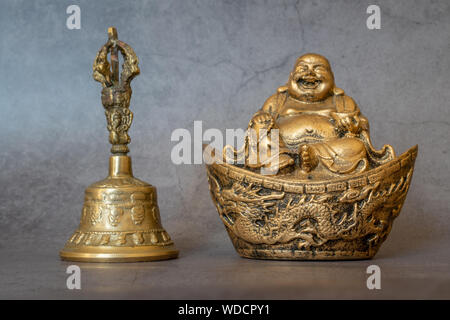 Figurina allegro Hotei e golden bell close-up, calmante e meditativa. Buddha Sorridente e golden bell isolato su sfondo grigio. Simboli di ASI Foto Stock