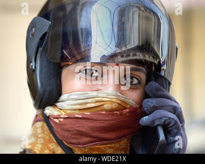 Giovani indiani del Rajasthan scooter ragazza con un parapolvere di protezione velo indossa un motociclo casco ed effettua una chiamata sul suo telefono cellulare. Foto Stock