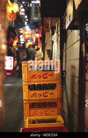 Impilati svuotato bottiglie in contenitori gialli a Omoide Yokocho cibo vicolo vicino a Shinjuku. Foto Stock