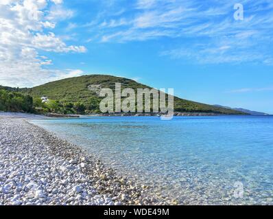 Estate sfondo. Mare calmo con acqua blu, ciottoli e cielo molto nuvoloso al mattino Foto Stock