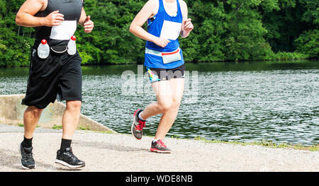Un uomo e una donna sono in esecuzione le une accanto alle altre nel bosco passando da un lago su un percorso sterrato. Foto Stock