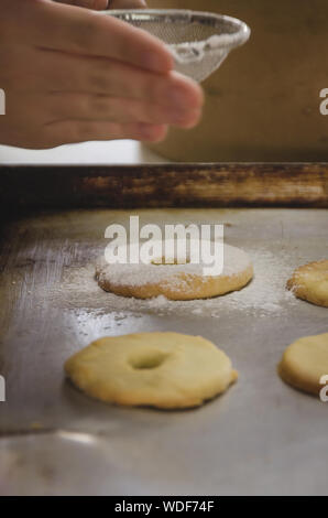 In verticale vicino la vista dei bambini mani spolverata di zucchero sulla parte superiore dei biscotti fatti in casa su una rustica fontana. Panificio scena Foto Stock