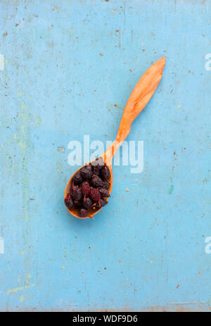 Rosa appassita hips in un cucchiaio di legno sul vecchio sfondo blu. Ingrediente per la cottura di bevanda salutare. Il concetto di rustico la terapia a base di erbe. Ingredi Foto Stock