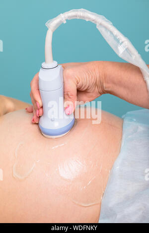 Ecografista la scansione di giovane donna incinta di addome con trasduttore a ultrasuoni esecuzione di ostetricia gravidanza o procedura di ultrasuoni Foto Stock