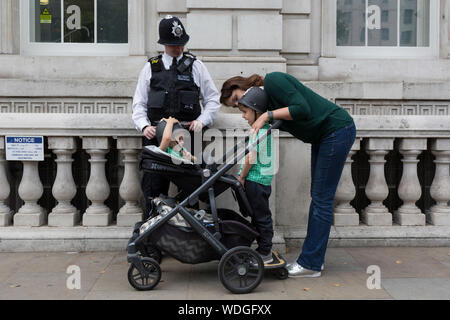 Due giovani ragazzi di plastica che indossa caschi di polizia sono reso felice da una vita reale funzionario di polizia al di fuori del Cabinet Office su Whitehall a Westminster, il 28 agosto 2019, a Londra, in Inghilterra. Foto Stock