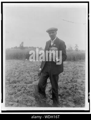 George Washington Carver, ritratto a figura intera, in piedi in campo, probabilmente a Tuskegee, tenendo pezzo di terreno Abstract/medio: 1 stampa fotografica. Foto Stock