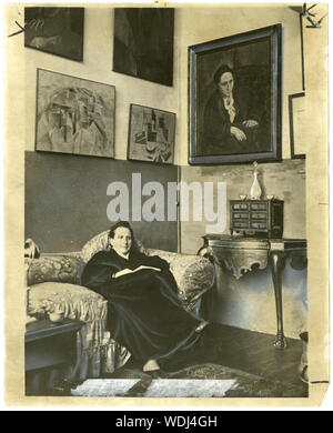 Gertrude Stein seduto su un divano nel suo studio di Parigi, con un ritratto di lei da Pablo Picasso e altri dipinti di arte moderna appesi al muro dietro di lei Foto Stock