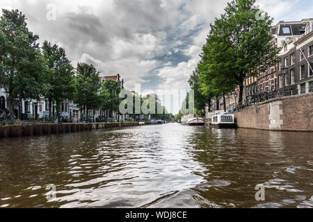 Amsterdam, Paesi Bassi - 30 Giugno 2019: Bianco grigio cloudscape con patch blu sopra canale Prinsengracht con verdi alberi lungo le pareti. Alcuni b Foto Stock