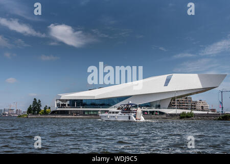 Amsterdam, Paesi Bassi - 30 Giugno 2019: Bianco occhio Museo dei film sotto il cielo blu con alcune nuvole bianche. IJ acqua nella parte anteriore. Imbarcazione da diporto in transito. Foto Stock