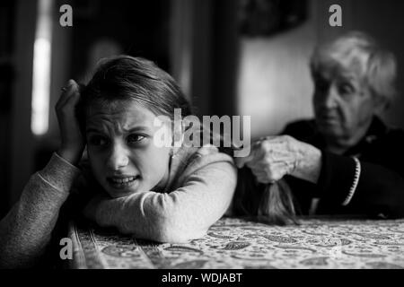 Vecchia donna trecce il suo pronipote di capelli. Foto in bianco e nero. Foto Stock