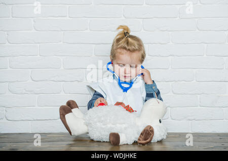 Il bambino gioca medico con toy pecore sul muro bianco. Baby veterinario esamina toy animale con stetoscopio. Futura professione concetto. Gioco, sviluppo, ho Foto Stock