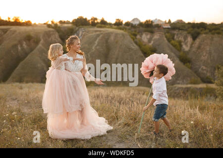 Elegante ragazzo dà un grande fiore a sua madre in un campo al tramonto. Foto Stock