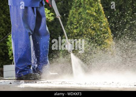 Uomini caucasici lavaggio viale di casa utilizzando la rondella a pressione. Tecnologie di pulitura. Foto Stock