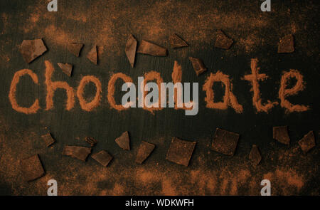 Iscrizione al cioccolato con il cacao in polvere con aggiunta di pezzi di cioccolato e cioccolato in polvere su di un nero lo sfondo di grafite Foto Stock