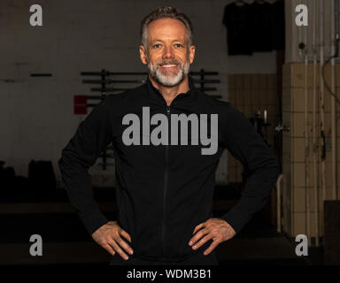 Ritratto di un attraente montare l uomo di mezza età in un fitness studio. Barbuto dai capelli grigi uomo con nero felpa sta cercando la fotocamera. Foto Stock