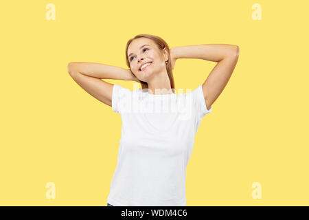 Giovani caucasici donna di mezza lunghezza verticale sul giallo di sfondo per studio. Bellissimo modello femminile in camicia bianca. Concetto di emozioni umane, l'espressione del viso. Guarda fiducioso, riposo, sognando. Foto Stock