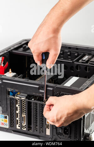 Le mani lo svitamento di una staffa della scheda video mentre la manutenzione hardware del personal computer con il fuoco selettivo closeup Foto Stock