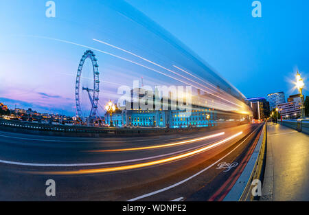 Paesaggio di Londra al blue ora, vista dal ponte di Westminster sull'occhio ruota e tracce di auto sulla strada, in Inghilterra, Regno Unito Foto Stock