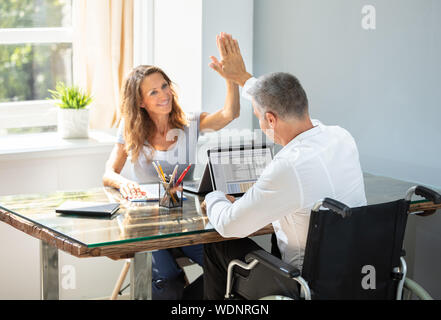Imprenditore disabili dando alta cinque al suo sorridente Partner femminile in Office Foto Stock