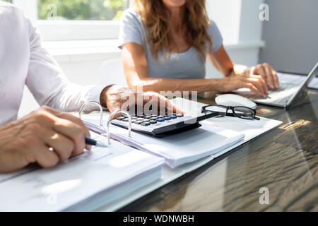 Sezione intermedia di due lavoratori relazione di calcolo mentre si lavora insieme in ufficio Foto Stock