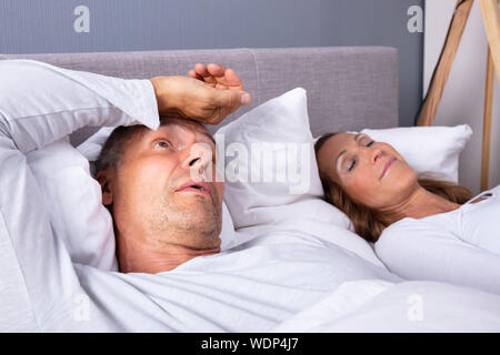Close-up di uomo maturo con insonnia giacente sul letto accanto alla moglie a casa Foto Stock