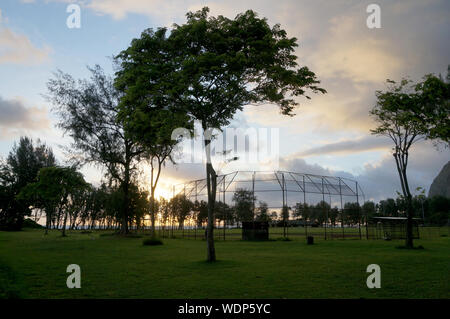 Alba sul campo in erba utilizzato per il baseball e il calcio al distretto di Waimanalo Beach Park con alberi e oceano in background. Foto Stock