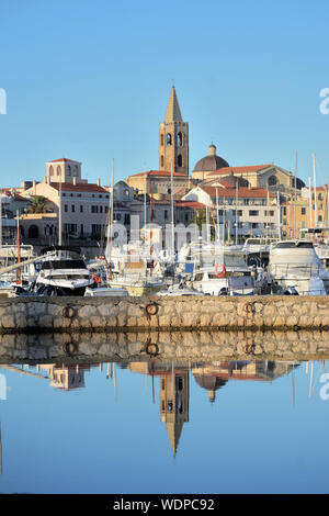 Vista panoramica della città di Alghero con il campanile del duomo in evidenza e la sua riflessione sull'acqua del porto Foto Stock