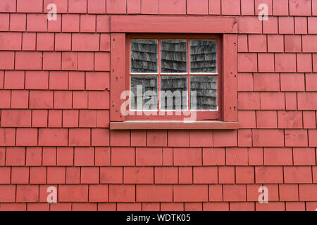 Piccola vecchia finestra in legno sulla parte esterna di un rosso parete shingle Foto Stock