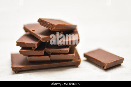Barra di cioccolato impilati sul bianco sullo sfondo di legno / close up pezzetti di cioccolato candy dessert e snack , il fuoco selettivo Foto Stock