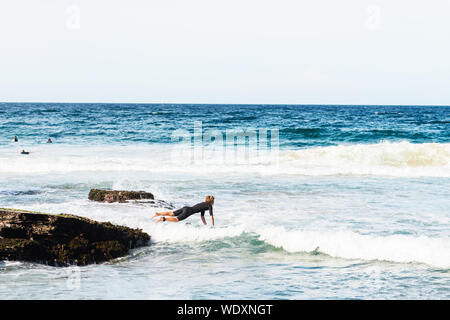 Giovani surfer jumping nell'oceano Rocks off Foto Stock