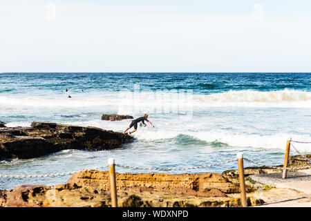 Giovani surfer jumping nell'oceano Rocks off Foto Stock