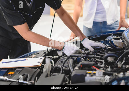 Asian maschio meccanico automatico esaminare auto motore guasto problema nella parte anteriore del veicolo automobilistico auto cappuccio femmina con il cliente. Sicurezza inspectio tecnico Foto Stock