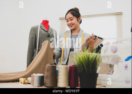 Designer di moda stilista nel proprietario di business workshop con il tablet e il cliente elenco contatti. Sarto e cucire concetto. Ritratto di felice alla moda casual fas Foto Stock