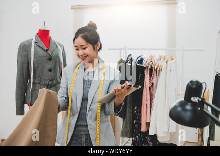 Designer di moda stilista nel proprietario di business workshop con il tablet e il cliente elenco contatti. Sarto e cucire concetto. Ritratto di felice alla moda casual fas Foto Stock