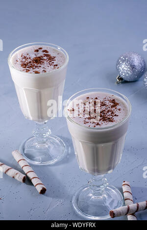 Due zabaione artigianale frappè con cannella, decorazioni di Natale su una texture di sfondo blu. Atmosfera natalizia. Foto Stock
