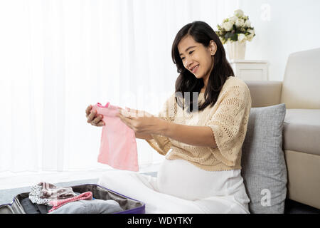 Asian donna incinta scegliere alcuni vestiti per il suo bambino Foto Stock