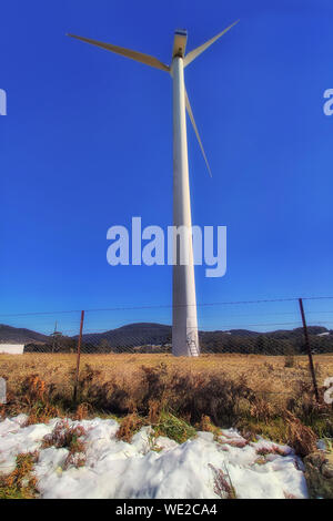 Il bianco della neve nelle montagne blu durante la stagione invernale attorno a turbina eolica su una proprietà remota contro il blu intenso del cielo. Insolitamente freddo inverno australiano o Foto Stock