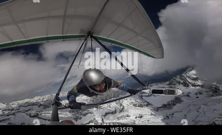 Deltaplano volare pilota con la sua ala in alta quota tra le nuvole sopra la neve picchi di montagna. Sport estremo. Foto Stock