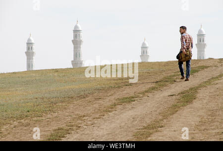 Uomo che cammina verso la Hazrat la Moschea del Sultano in Nur-Sultan, Kazakistan, mentre solo il quattro minareti può essere visto a ridosso di una collina. Foto Stock
