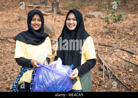 Due donna hijab volontario sorridente holding borsa cestino in posizione di parcheggio Foto Stock