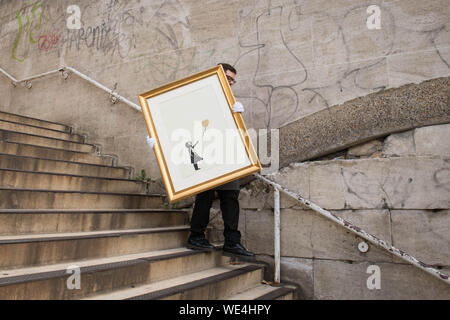 Dipendente della casa d'aste Christie's con una versione di ÔGirl with Balloon' dell'anonimo Street artist Banksy, vicino a una delle sedi in cui l'opera apparve originariamente sulla Southbank a Londra. La foto è dovuta essere venduto in un'asta online, ÔBanksy: Non posso credere che si moroni effettivamente acquistare questo sh*t' che si svolgerà dal 11 al 24 settembre. Foto Stock