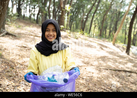 Il hijab donna sorridente volontario azienda borsa cestino in posizione di parcheggio Foto Stock