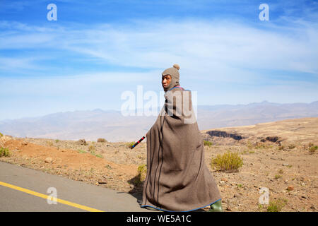 Seforong, Lesotho - Settembre 19, 2017 African giovane pastore uomo in nazionale coperta di lana e Abbigliamento Passamontagna cappuccio va lungo zone rurali ad alta strada di montagna Foto Stock